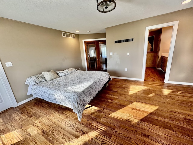 bedroom featuring french doors, a textured ceiling, visible vents, wood finished floors, and baseboards