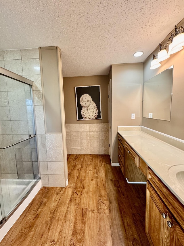full bath featuring wood finished floors, a textured ceiling, a shower stall, and tile walls
