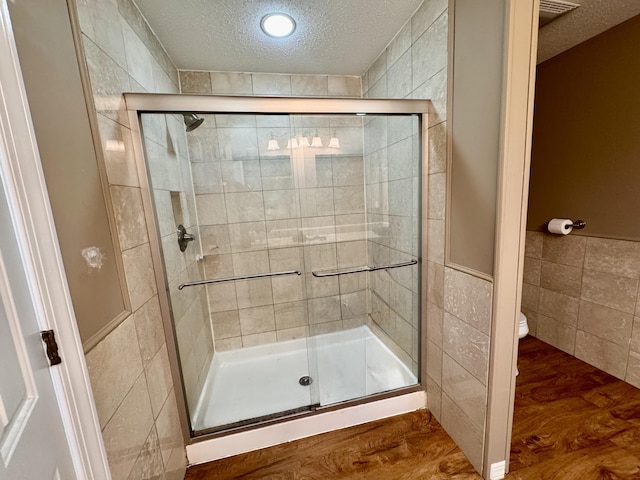 bathroom featuring a textured ceiling, a stall shower, toilet, and tile walls