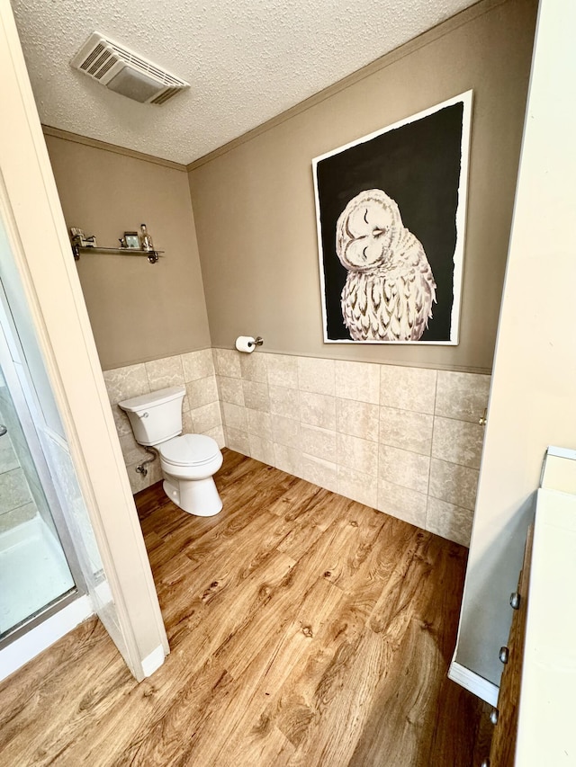 bathroom featuring tile walls, wainscoting, wood finished floors, and visible vents