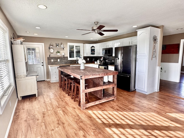 kitchen featuring range with electric stovetop, white cabinets, stainless steel microwave, black refrigerator with ice dispenser, and light wood-style floors