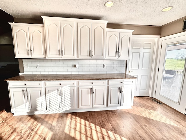 kitchen featuring white cabinets, a textured ceiling, tasteful backsplash, and light wood-style floors