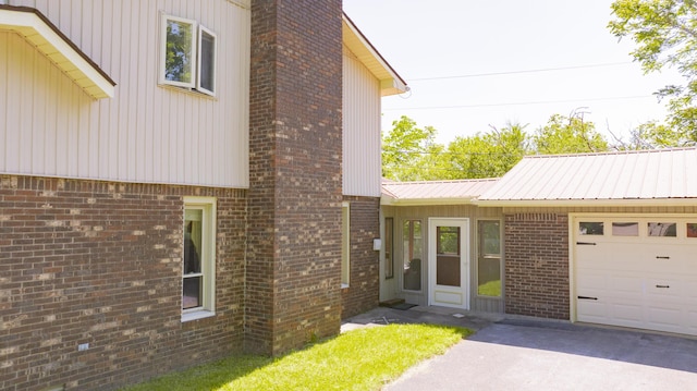 exterior space featuring concrete driveway, brick siding, an attached garage, and metal roof