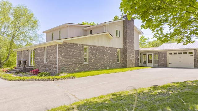 view of property exterior with an attached garage, brick siding, driveway, and a chimney