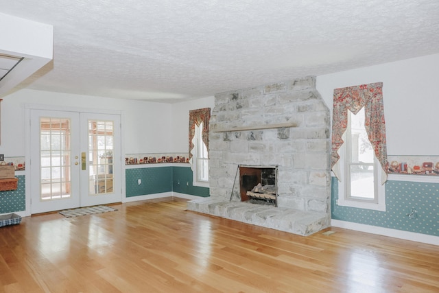 unfurnished living room with a healthy amount of sunlight, a textured ceiling, french doors, and wood finished floors