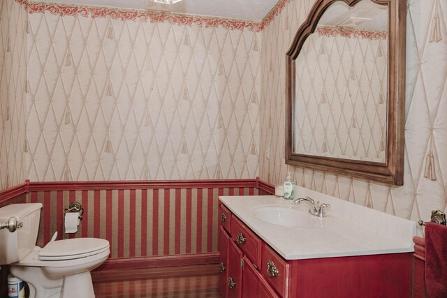bathroom featuring toilet, wallpapered walls, and vanity