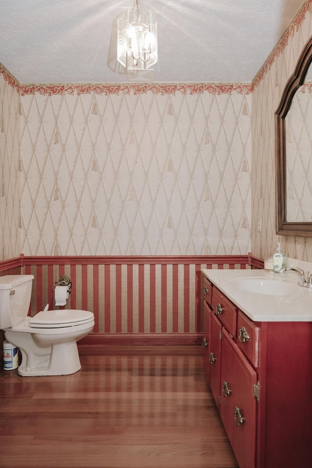 half bath with toilet, wallpapered walls, wood finished floors, and vanity
