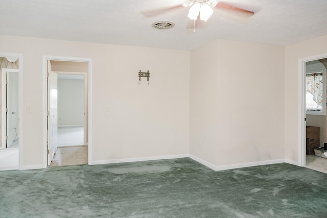 empty room with carpet flooring, a ceiling fan, baseboards, and visible vents