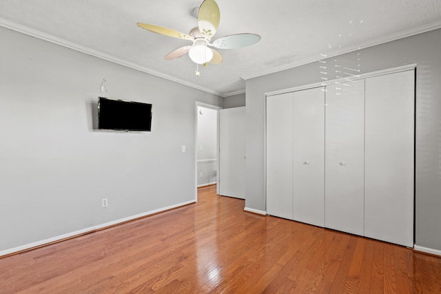 unfurnished bedroom featuring crown molding, a closet, wood finished floors, baseboards, and a ceiling fan