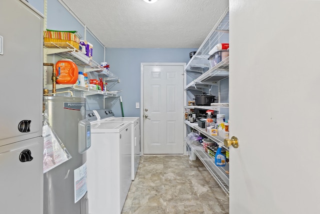 laundry area featuring laundry area, a textured ceiling, stone finish floor, water heater, and washer and clothes dryer
