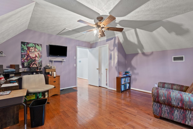 office space featuring ceiling fan, visible vents, baseboards, wood finished floors, and vaulted ceiling