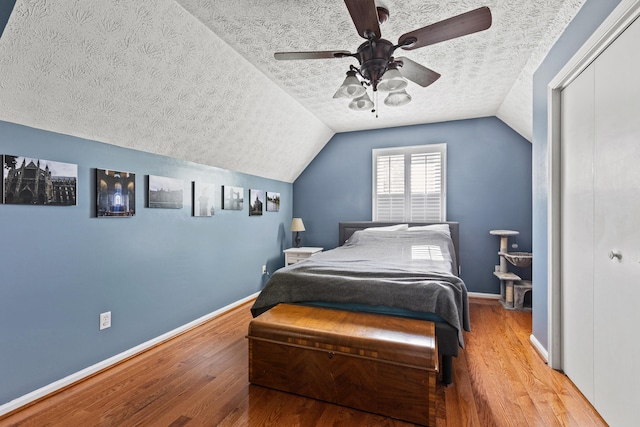 bedroom featuring a textured ceiling, vaulted ceiling, baseboards, and wood finished floors