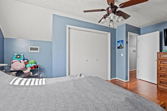 bedroom with a ceiling fan, a textured ceiling, visible vents, wood finished floors, and a closet