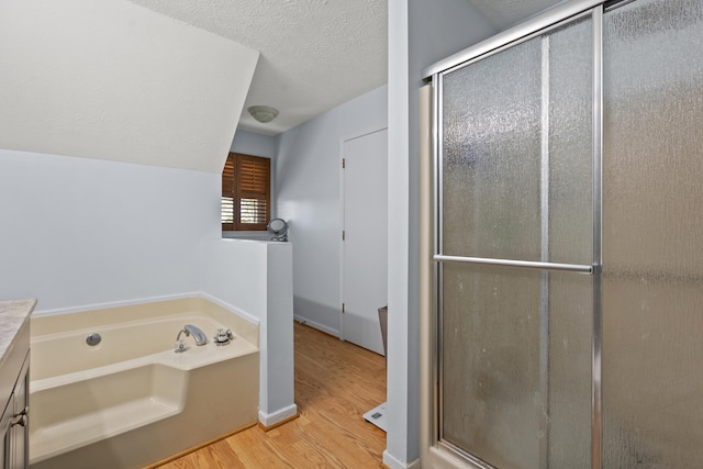 full bathroom with a textured ceiling, a bath, a shower stall, wood finished floors, and vanity