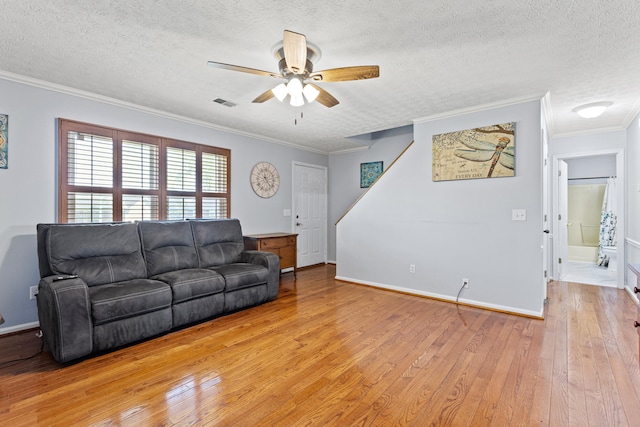 living area featuring ceiling fan, light wood-style floors, a textured ceiling, visible vents, and ornamental molding