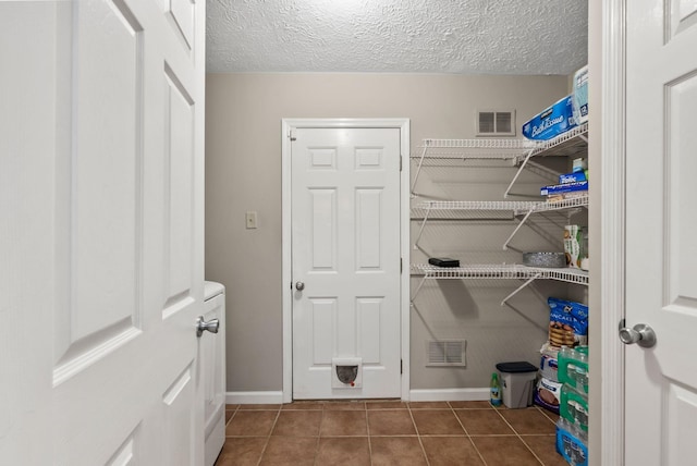 laundry area featuring laundry area, a textured ceiling, tile patterned flooring, and visible vents