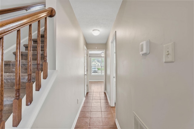 corridor featuring baseboards, stairs, a textured ceiling, and light tile patterned floors