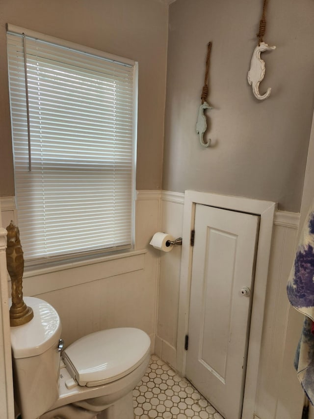 half bathroom featuring a wainscoted wall, tile patterned flooring, a decorative wall, and toilet