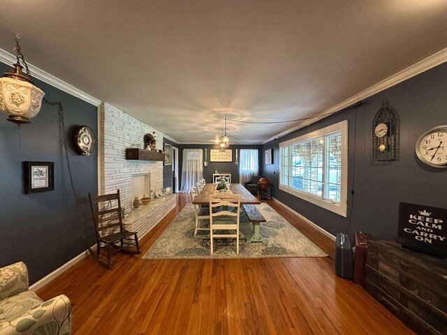 dining room with crown molding, baseboards, a brick fireplace, and wood finished floors