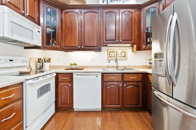 kitchen with a sink, light countertops, dark wood-style floors, glass insert cabinets, and white appliances
