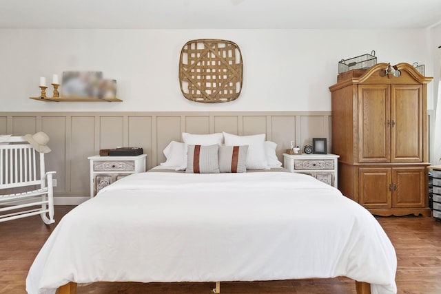 bedroom featuring a wainscoted wall, a decorative wall, and wood finished floors