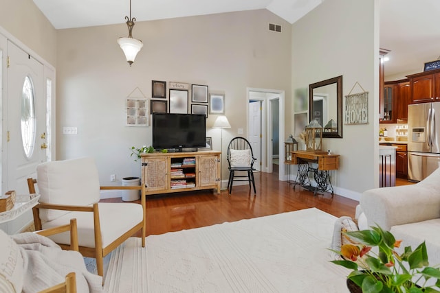 living room featuring visible vents, baseboards, wood finished floors, and high vaulted ceiling