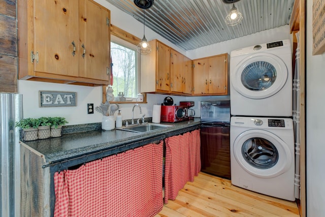 laundry area with light wood-type flooring, a sink, and stacked washer and dryer