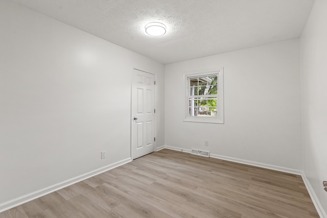 empty room with a textured ceiling, visible vents, baseboards, and light wood-type flooring