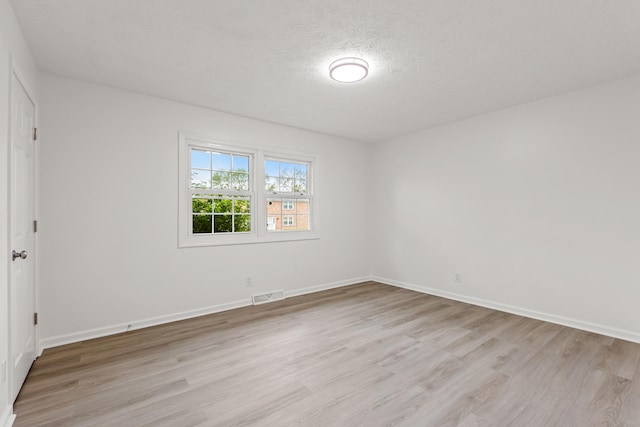 unfurnished room featuring a textured ceiling, baseboards, visible vents, and light wood finished floors