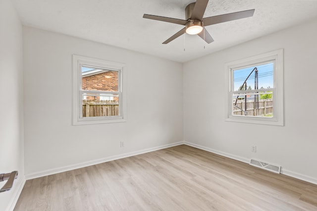 spare room with light wood-style floors, baseboards, ceiling fan, and visible vents