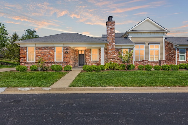 view of front of house featuring a chimney, brick siding, and a front yard