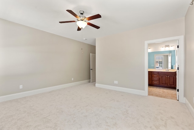 unfurnished bedroom featuring light carpet, baseboards, ceiling fan, a sink, and ensuite bath