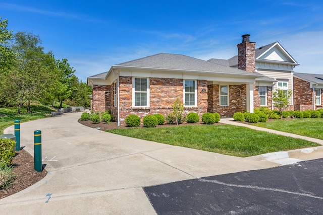 view of front of house featuring brick siding, a front lawn, driveway, and a chimney