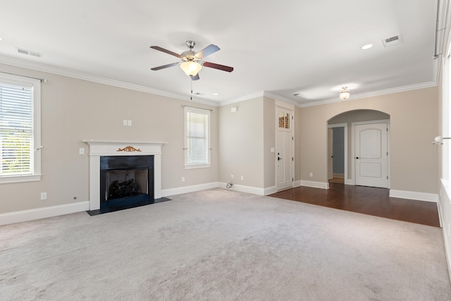 unfurnished living room featuring crown molding, carpet floors, arched walkways, a ceiling fan, and visible vents