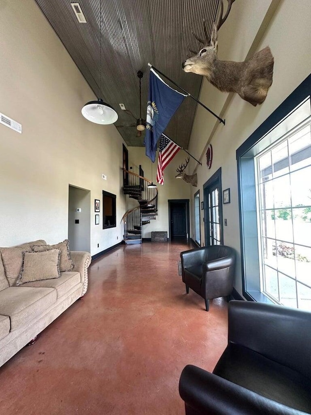 living area with a ceiling fan, visible vents, finished concrete flooring, a high ceiling, and stairs