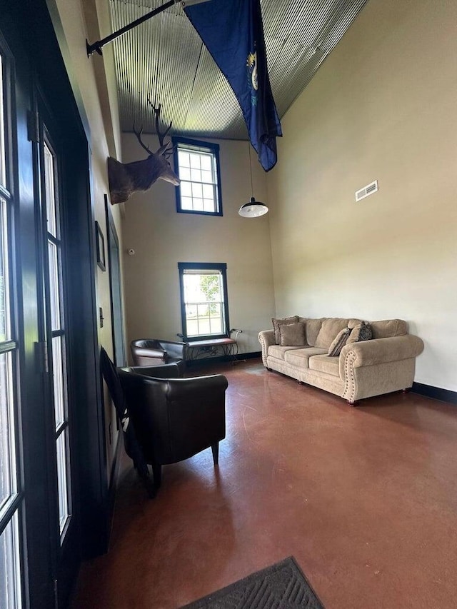 living area with a high ceiling, visible vents, baseboards, and finished concrete floors