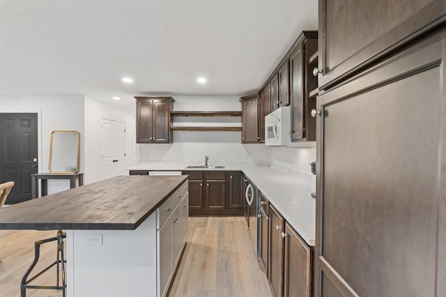 kitchen with a sink, open shelves, light wood-type flooring, white microwave, and a center island