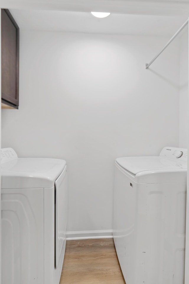 laundry room featuring washing machine and dryer, cabinet space, light wood finished floors, and baseboards