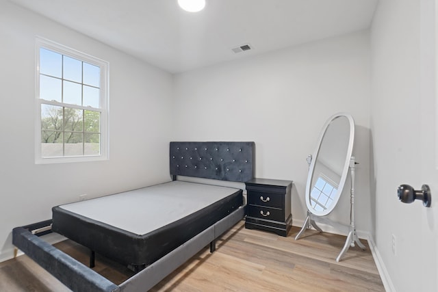 bedroom with multiple windows, light wood-style floors, and baseboards