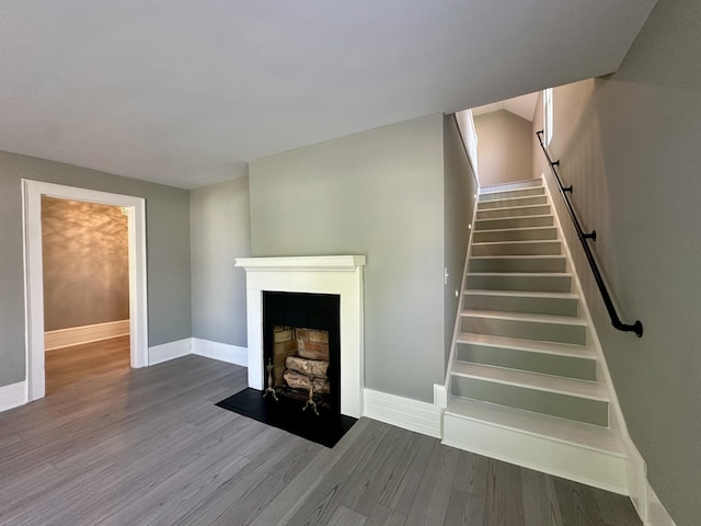 staircase featuring baseboards, a fireplace with flush hearth, and wood finished floors