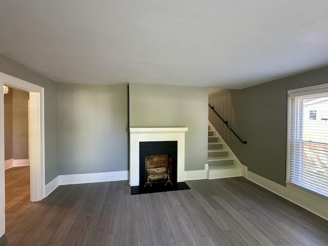 unfurnished living room with a fireplace with flush hearth, baseboards, stairs, and wood finished floors