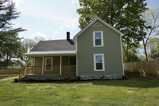 back of house with covered porch, a lawn, fence, and a shingled roof