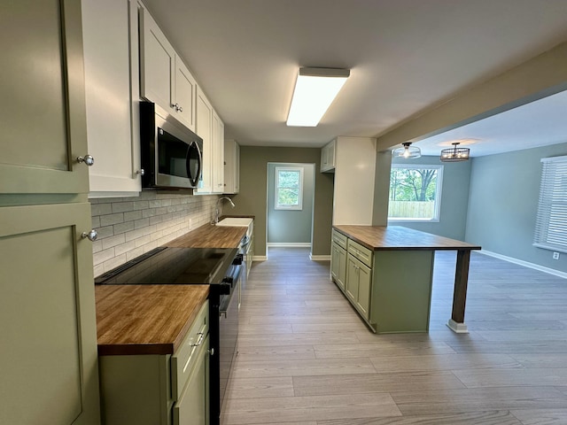 kitchen with black electric range oven, butcher block countertops, baseboards, stainless steel microwave, and tasteful backsplash