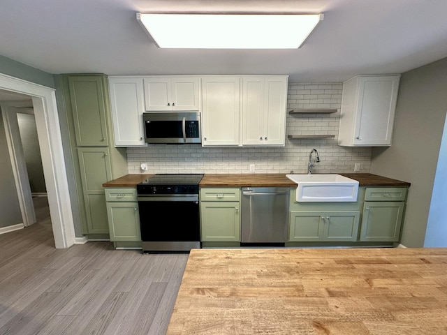 kitchen with open shelves, butcher block countertops, a sink, green cabinets, and stainless steel appliances