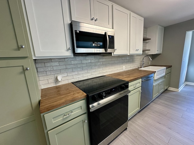 kitchen with butcher block countertops, a sink, green cabinets, stainless steel appliances, and light wood-style flooring