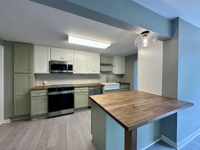 kitchen with a sink, wooden counters, stainless steel appliances, light wood-type flooring, and tasteful backsplash