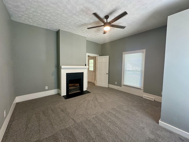 unfurnished living room with carpet flooring, a textured ceiling, a ceiling fan, a fireplace with flush hearth, and visible vents