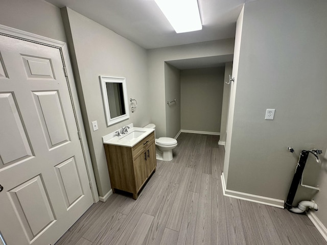 bathroom featuring toilet, baseboards, wood finished floors, and vanity