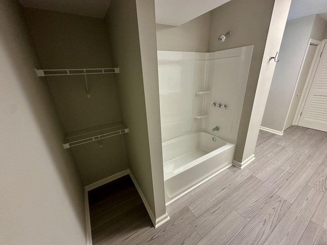 full bath featuring a walk in closet, baseboards, wood finished floors, and shower / bathing tub combination