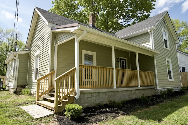 view of front of house featuring a porch, a shingled roof, and a chimney
